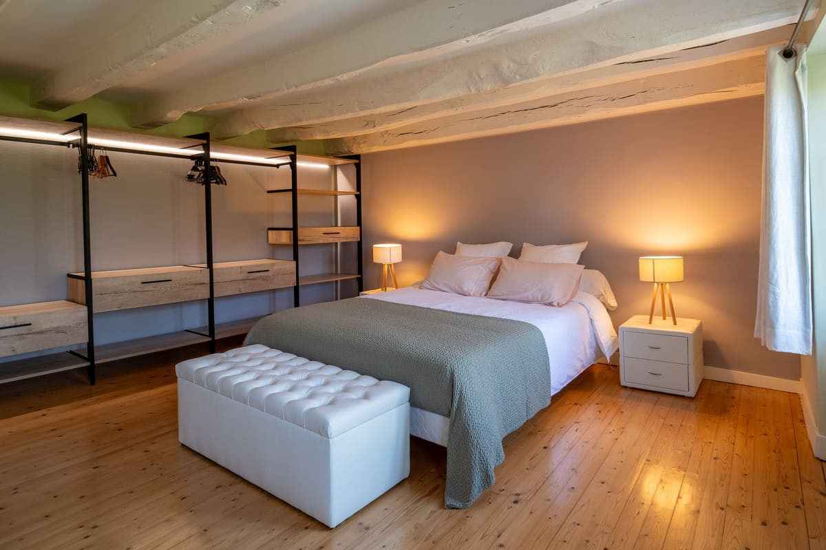 Chambre du Domaine la Roche avec lit double, banc capitonné et étagère en métal